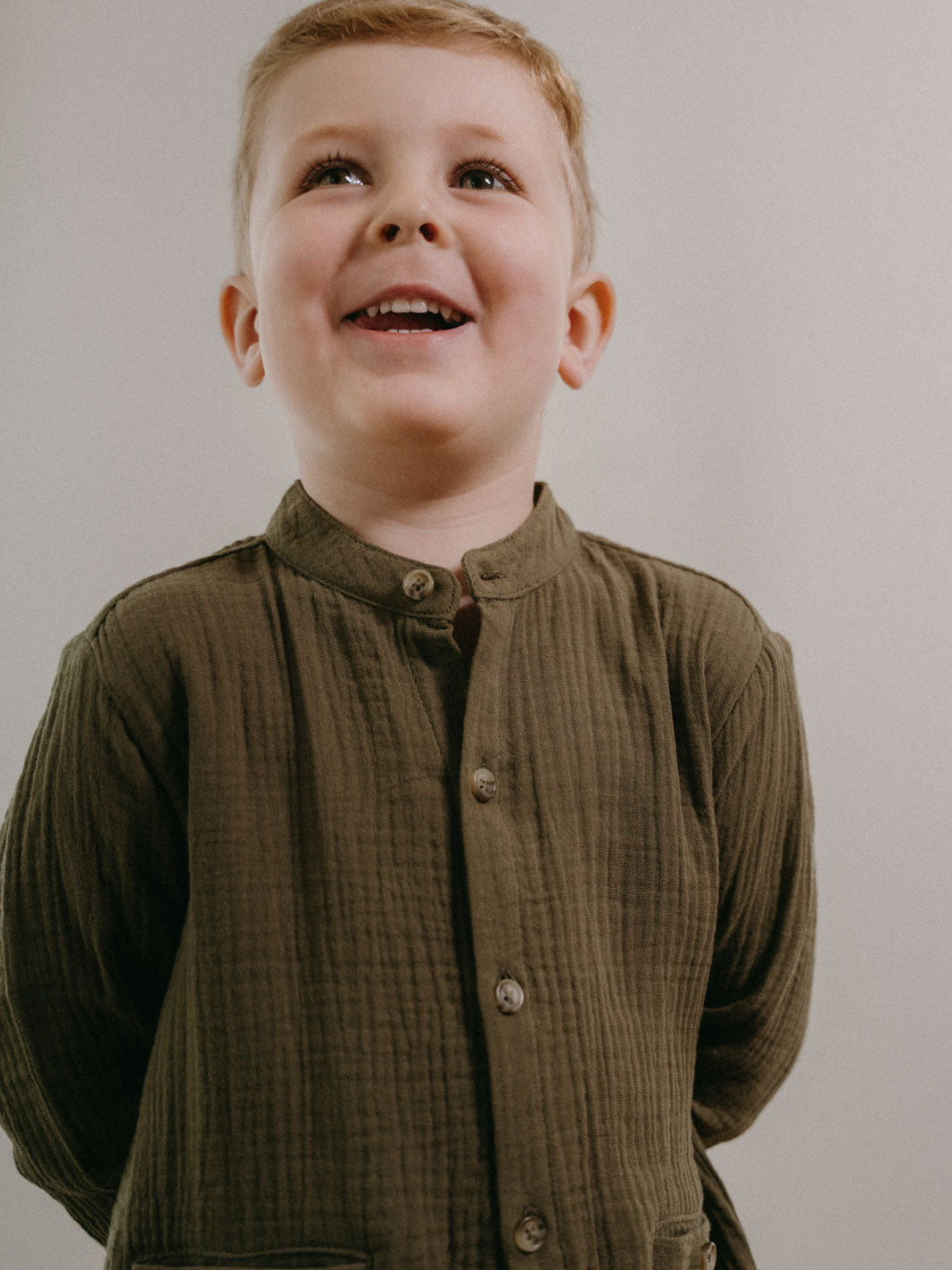 Young boy wearing an olive green button-up shirt looking upward Grandad Shirt - Forest Boys