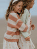 Two children hugging, one wearing a striped sweater and the other in a star-patterned dress, against a neutral background.