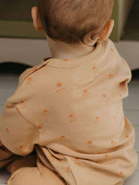 Baby wearing a light brown outfit with subtle patterns, sitting on a surface.