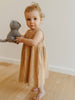 Child in a brown dress holding a gray stuffed animal on a wooden floor.
