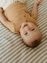 Baby lying on a striped bed wearing a brown outfit
