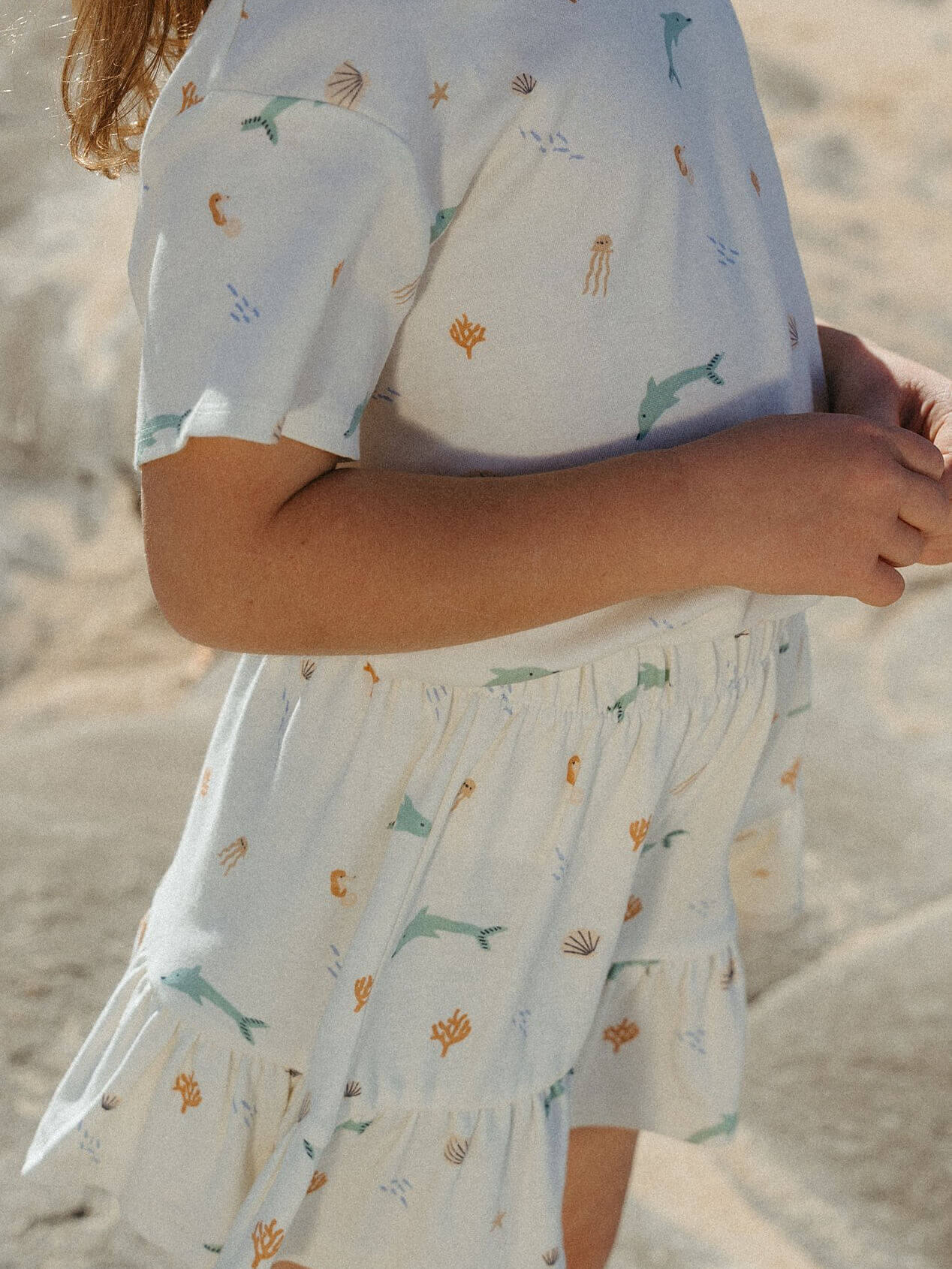 Girl wearing a light blue dress with animal prints on a sandy background