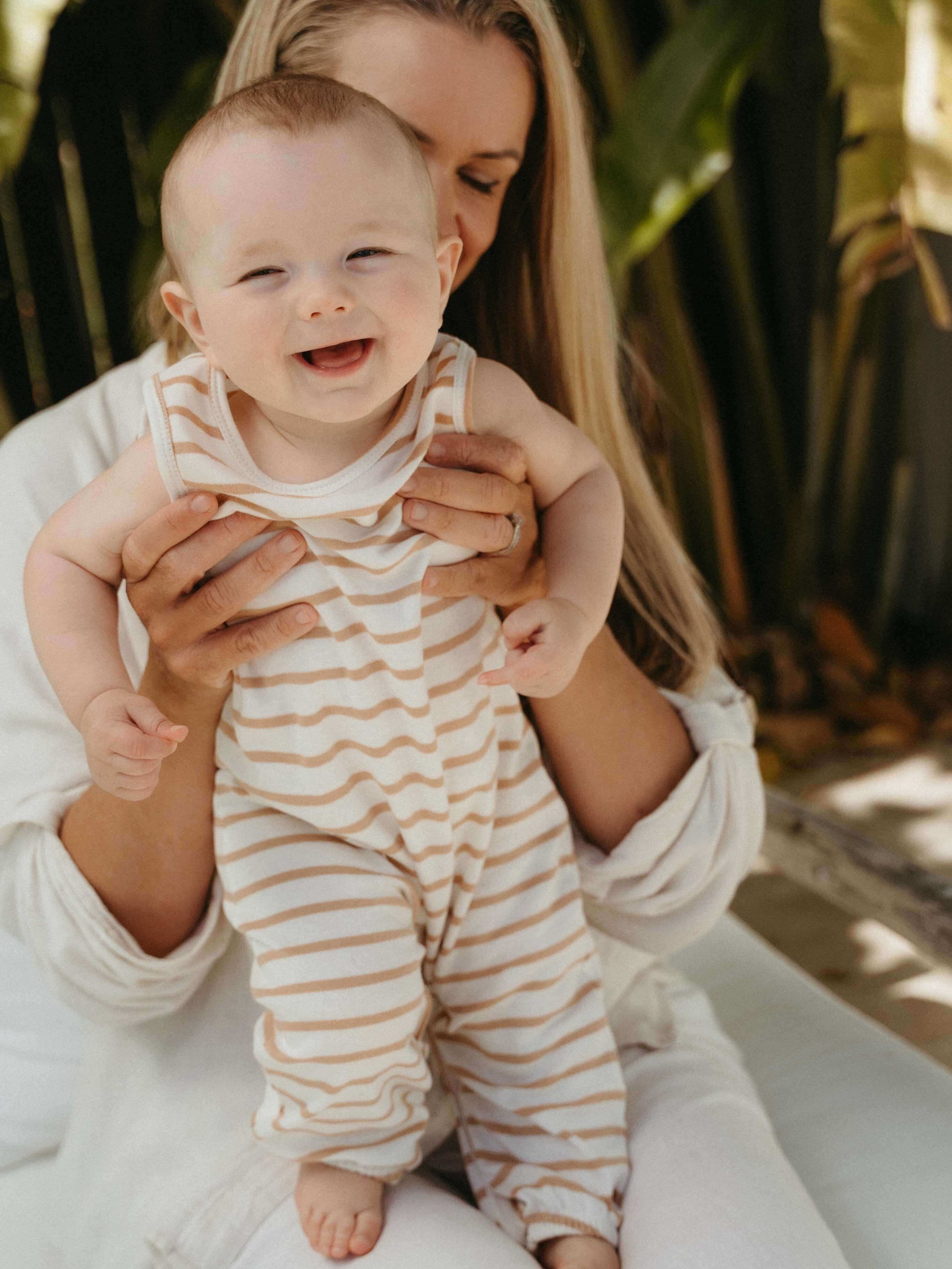 Woman holding a baby wearing a striped onesie with a blurred natural background