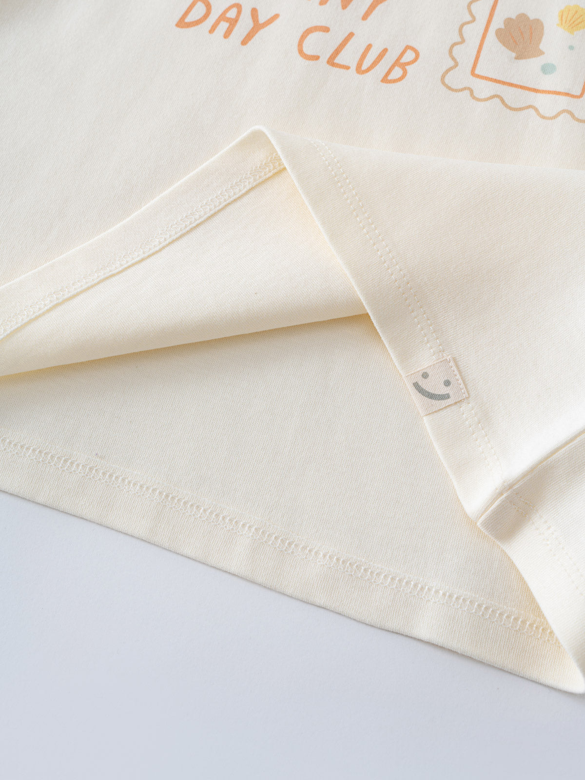 Close-up of a cream long sleeve shirt with embroidered details and smiling face tag Long Sleeve Tee - Sunny Club Day Girls