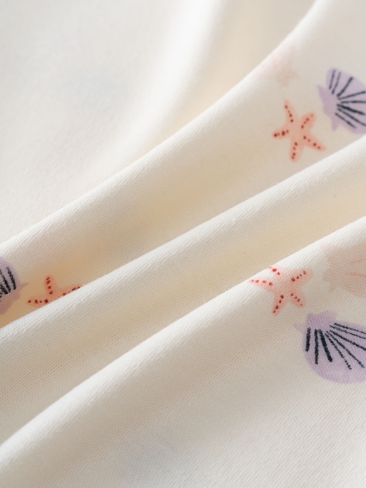 Close-up of cream fabric with purple shells and orange starfish print Lottie Short Sleeve Dress - Beach Shells Girls