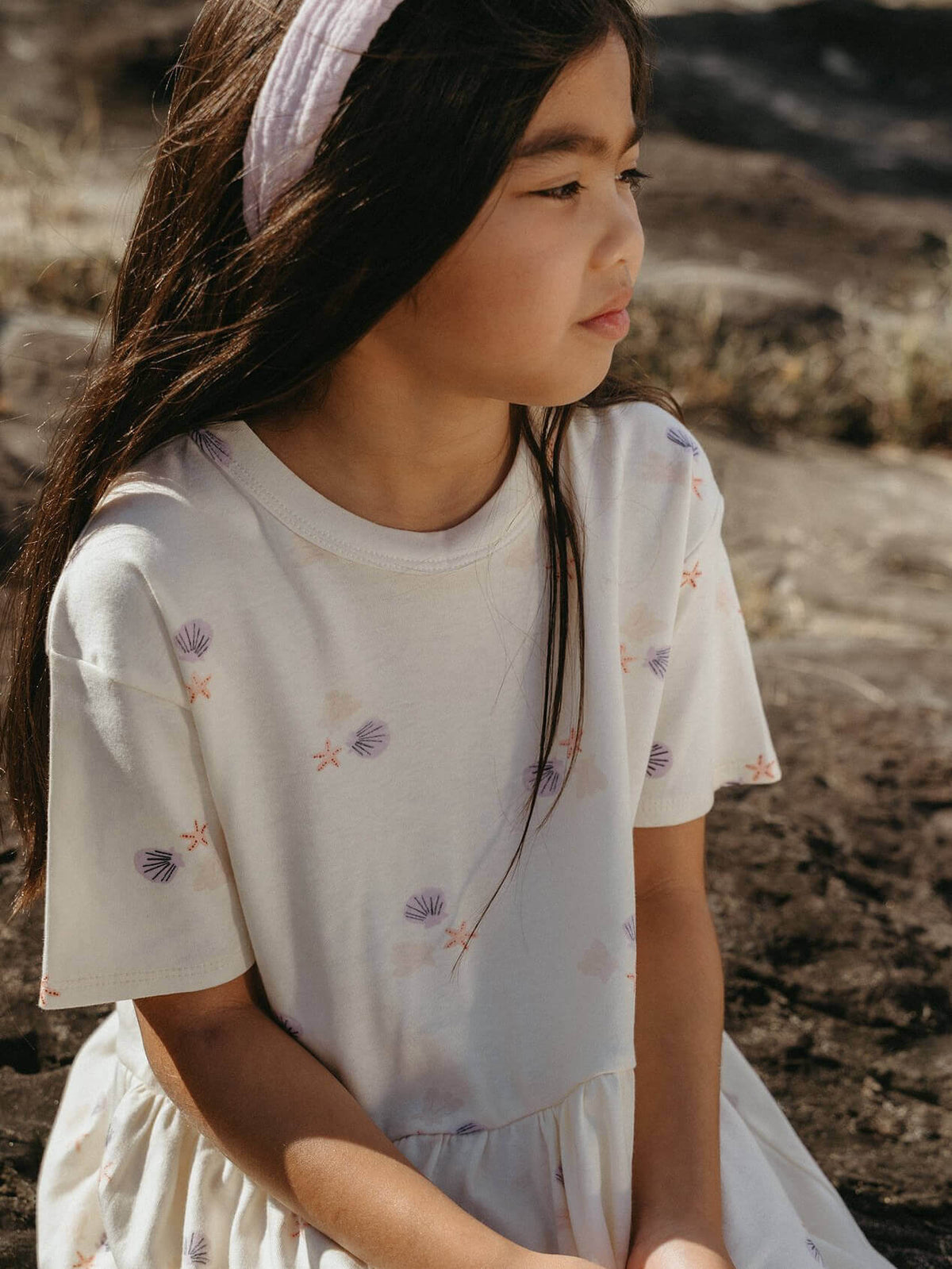 Young girl wearing a white dress with floral patterns in a natural setting Lottie Short Sleeve Dress - Beach Shells Girls