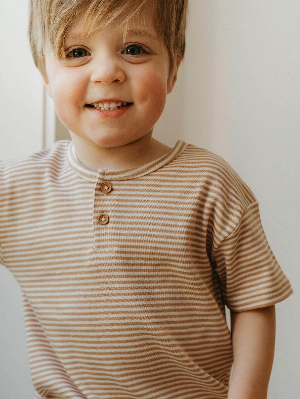 Child wearing a brown and white striped shirt with a neutral background