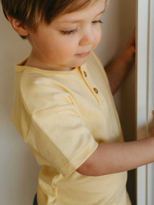 Child wearing a yellow shirt standing indoors.