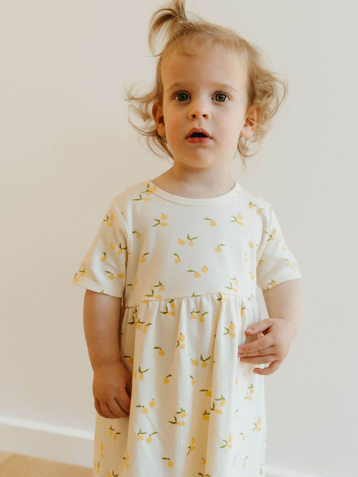 Child wearing a white dress with yellow patterns against a plain background