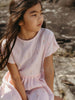 Young girl in a pink dress sitting outdoors on a natural background