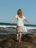 Girl in a dress standing on rocks by the ocean with arms outstretched