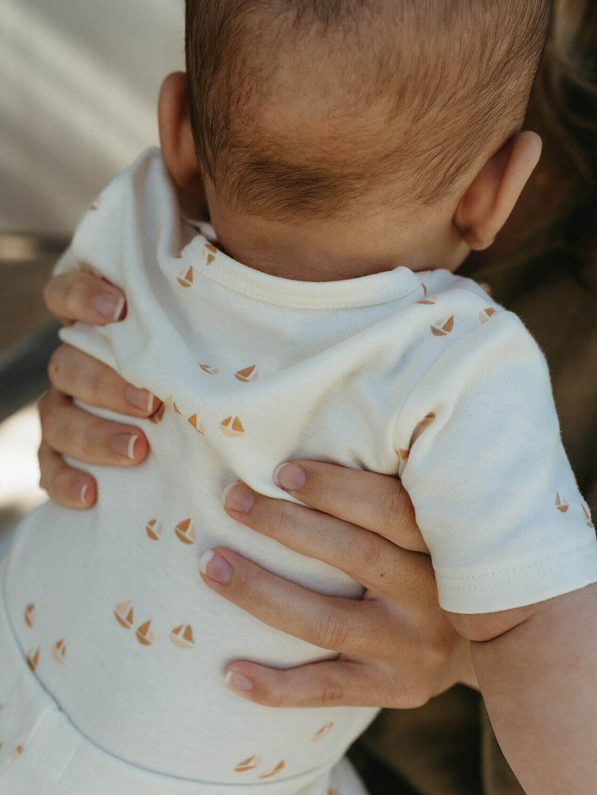 Person holding a baby wearing a white onesie with small patterns. Matt Short Sleeve Bodysuit - Sailing Baby boy