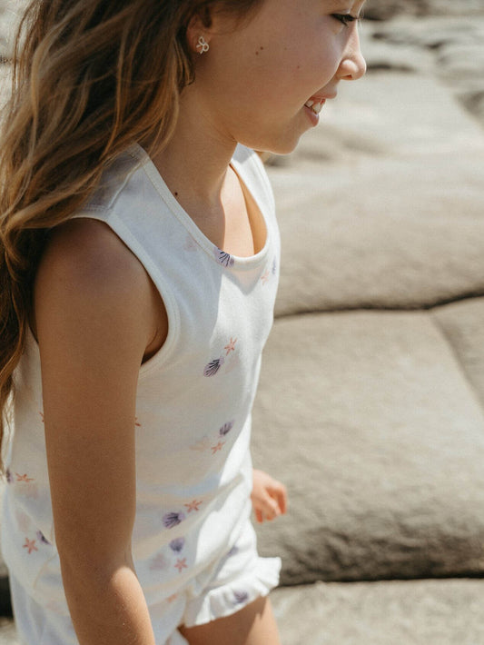 Young girl in a white sleeveless dress with floral patterns sitting on a stone surface.