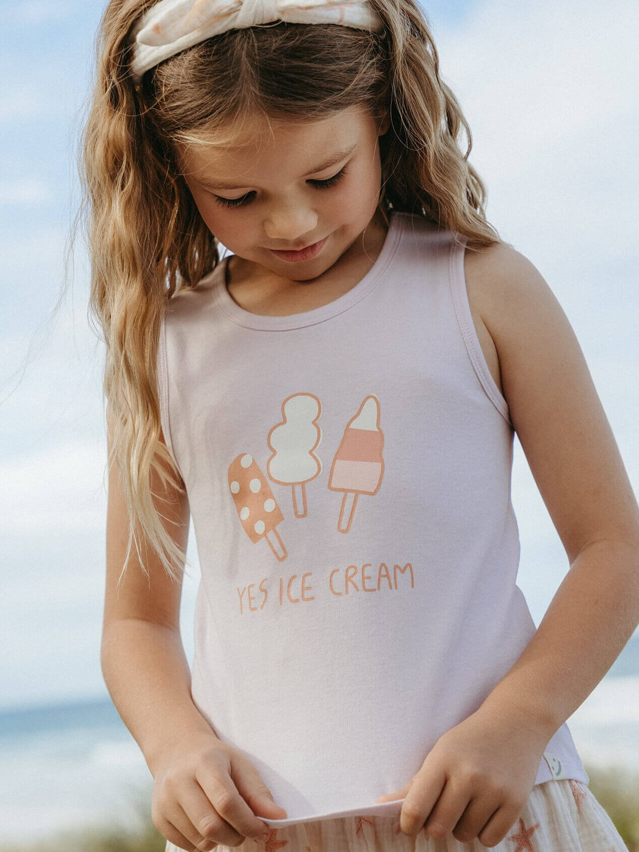 Young girl wearing a sleeveless shirt with ice cream graphics and text.