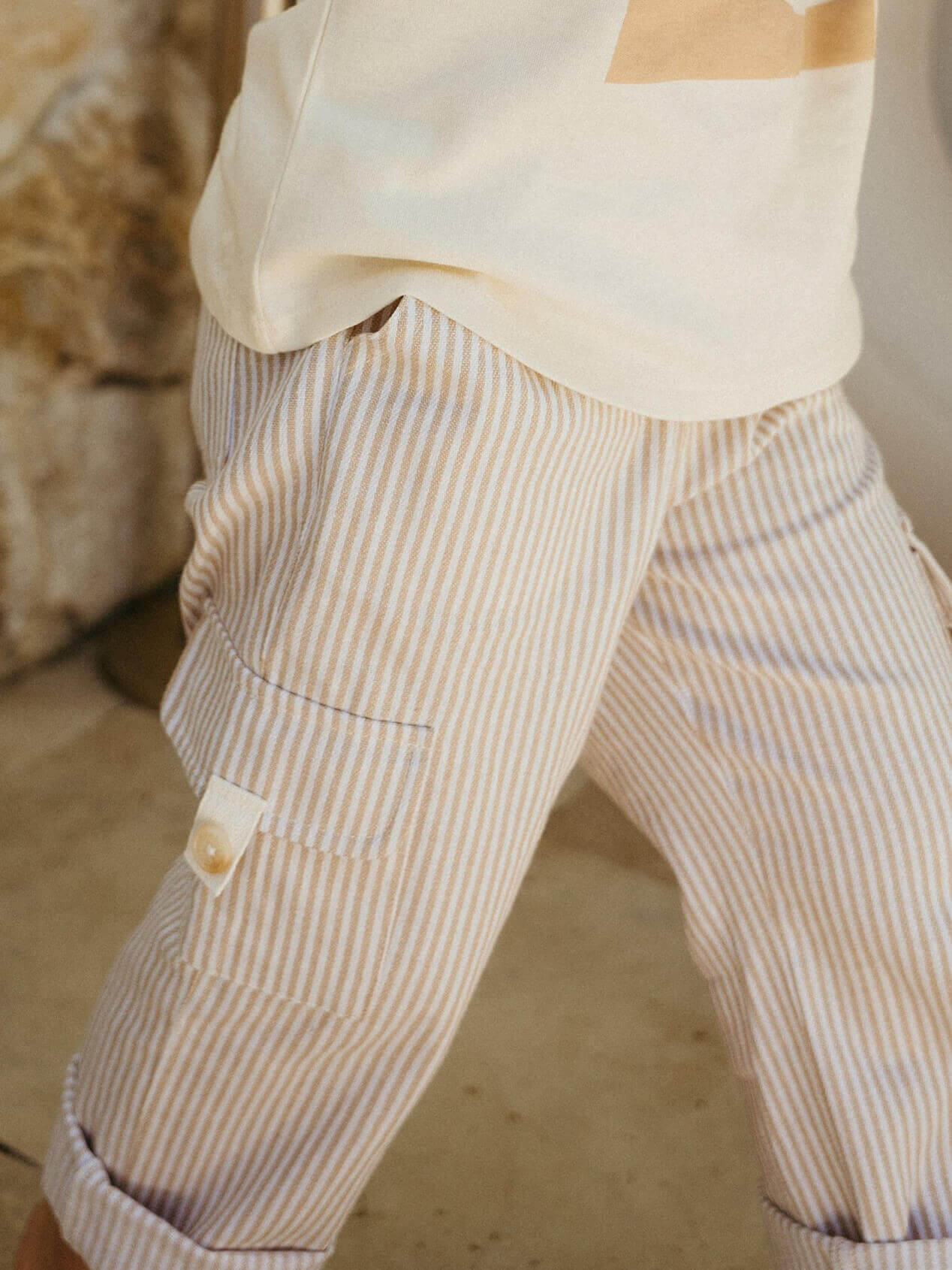 Close-up of a child wearing beige and white striped pants with a blurred background.