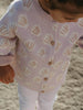 Child wearing a light purple cardigan with shell pattern on a sandy background