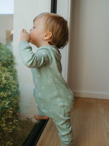 Child in a green onesie standing by a door