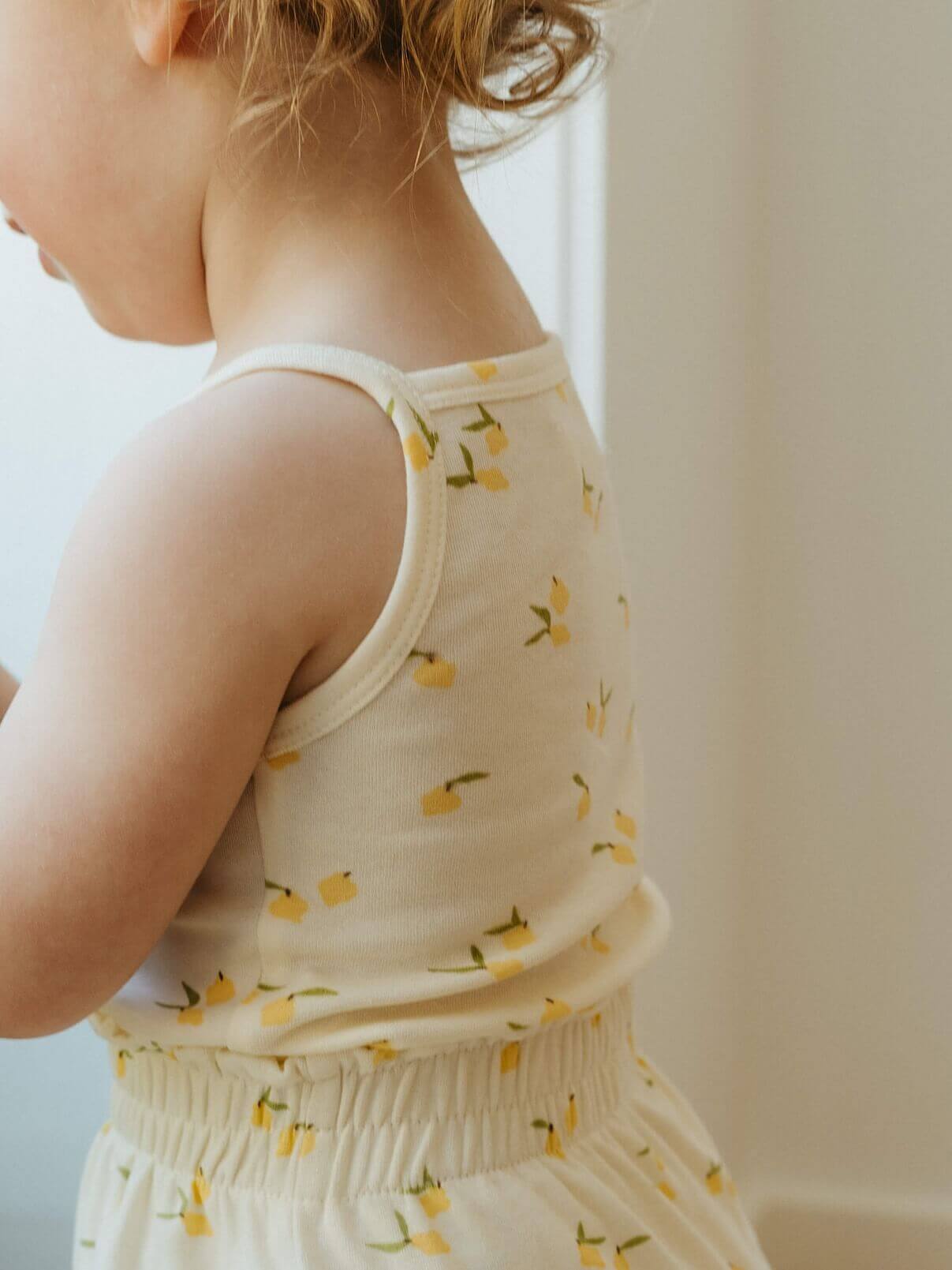 Child wearing a sleeveless top with lemon pattern against a neutral background