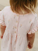 Close-up of a child wearing a pink dress with floral embroidery on a neutral background Muslin Dress - Poppy Field Girls