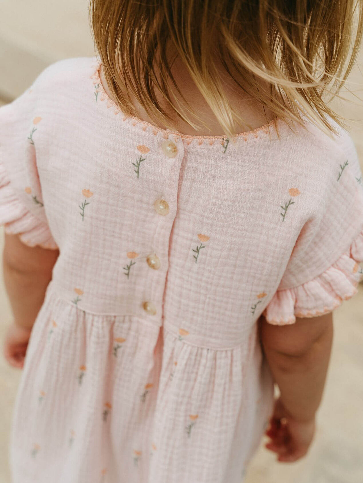 Close-up of a child wearing a pink dress with floral embroidery on a neutral background Muslin Dress - Poppy Field Girls