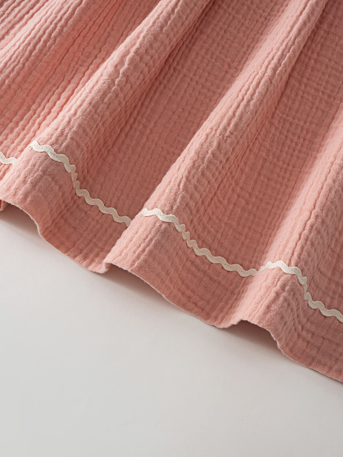 Close-up of pink textured fabric hem with white wavy trim detail muslin Dress - Toasted Peach Girls