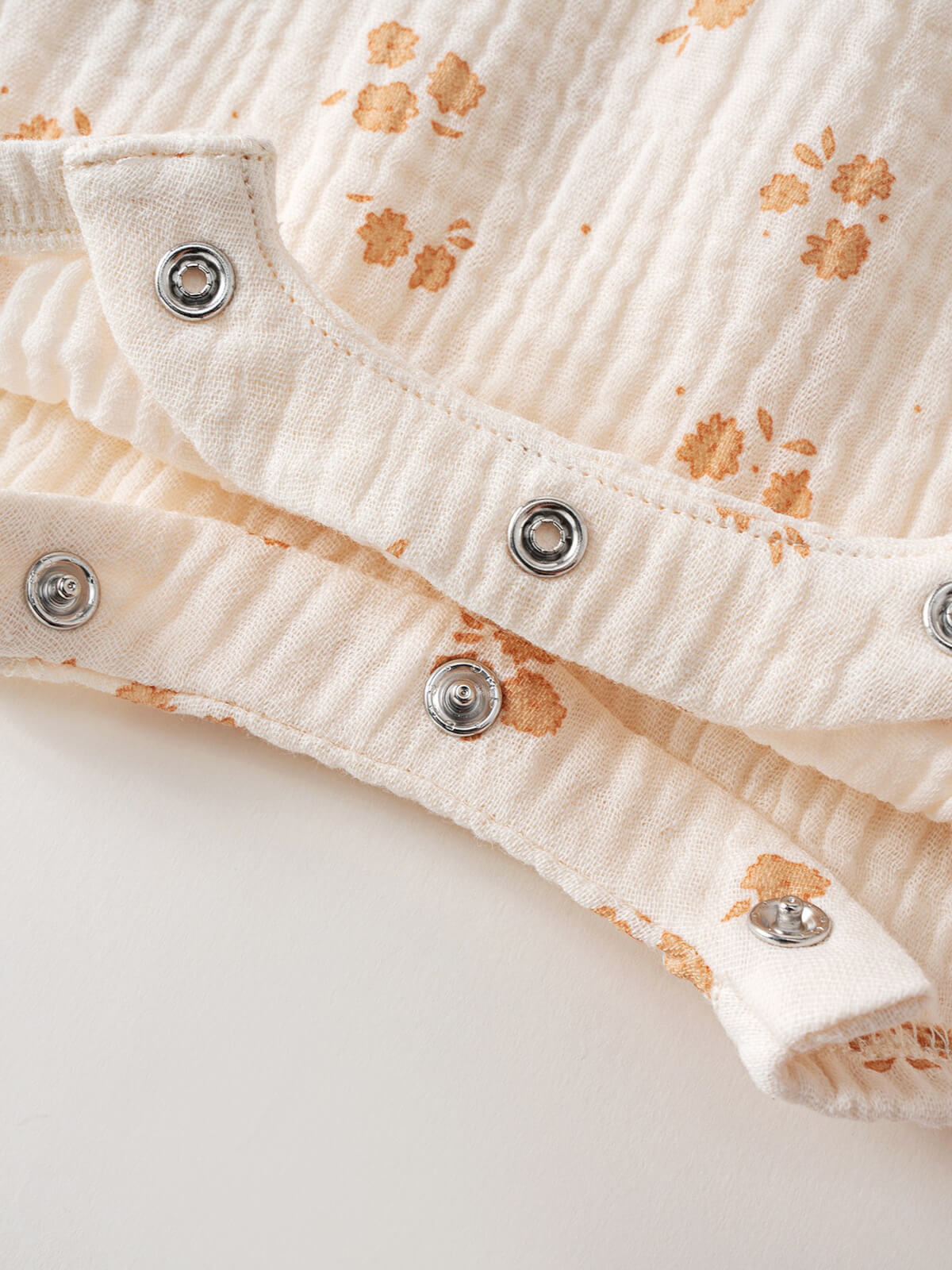 Close-up of cream ribbed fabric with orange paw prints and metal snap buttons Muslin Romper - Petal Paws Baby girl