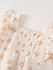 Close-up of white smocked baby romper with orange floral print and ruffled straps Muslin Romper - Petal Paws Baby girl