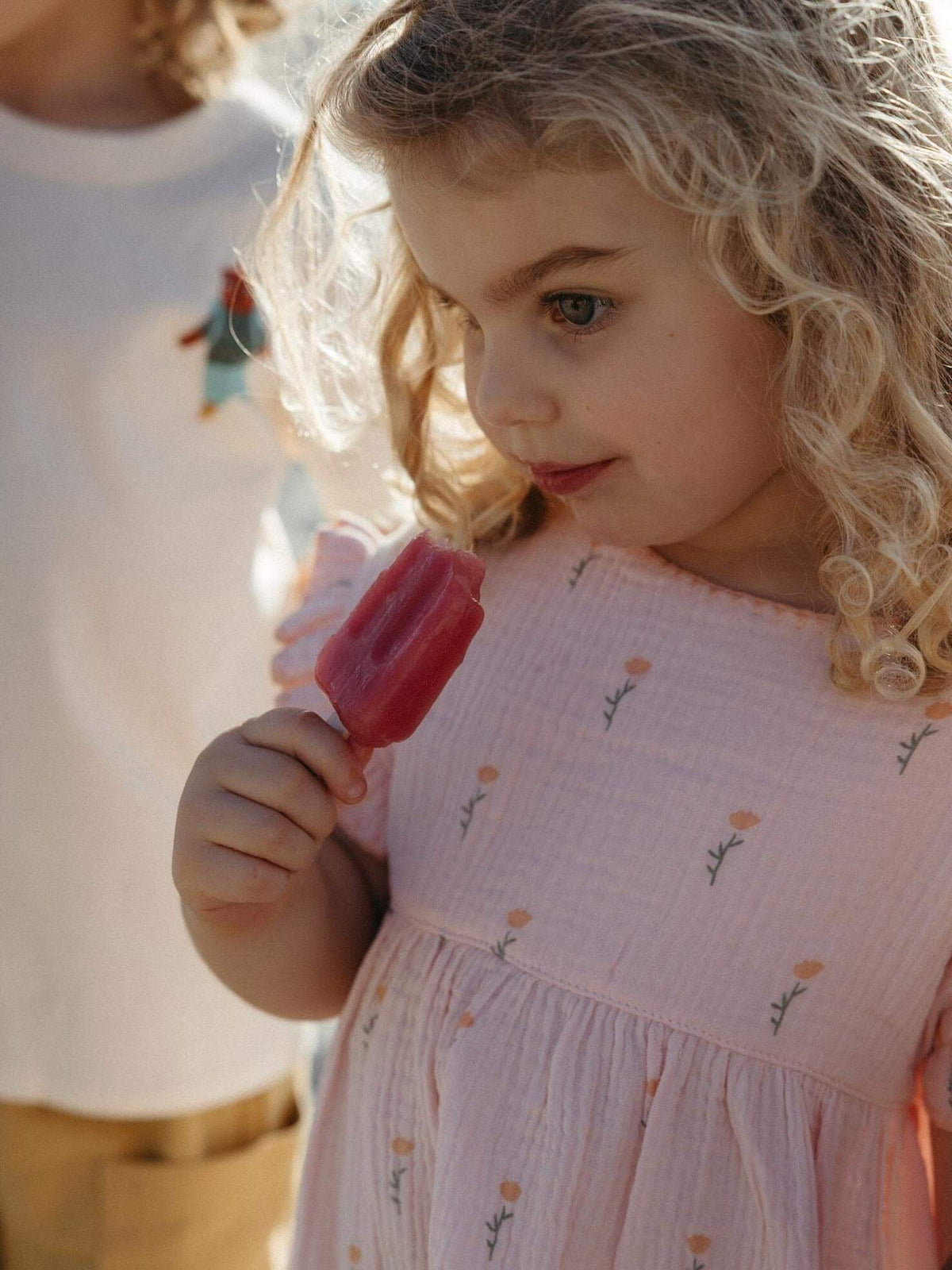 Girl having an ice block at the beach wearing a pink dress with flowers