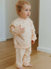 Child wearing a light pink outfit with small patterns indoors on a wooden floor.
