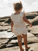 Child in a floral romper standing on rocky terrain near water