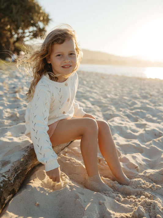 Girl at the beach playing with sand wearing a white pointelle cardigan