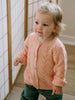 Child wearing a pink knitted sweater standing indoors. Pointelle Cardigan - Mallow Girls