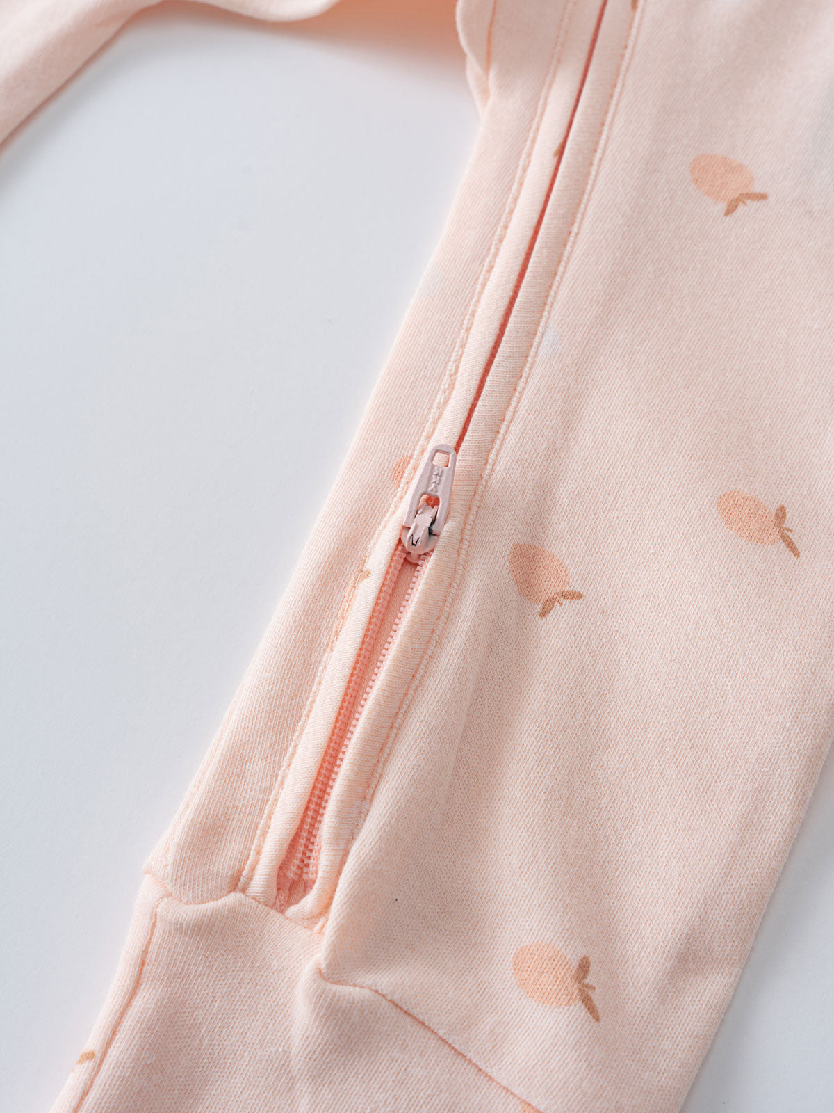 Close-up of a peach-colored baby garment with apple print and zipper detail Printed Long Sleeve One Piece - Apples Baby girl