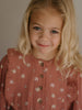 Young girl with blonde hair wearing a patterned dress against a neutral background Printed Woven Dress - Bird And Blossom Rosehip Girls
