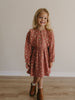 Young girl wearing a patterned dress standing on a wooden floor with a plain wall background Printed Woven Dress - Bird And Blossom Rosehip Girls