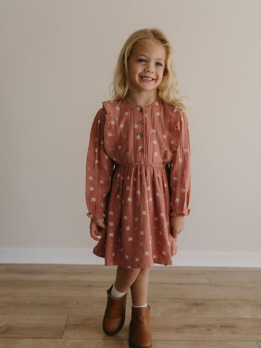 Young girl wearing a patterned dress standing on a wooden floor with a plain wall background Printed Woven Dress - Bird And Blossom Rosehip Girls