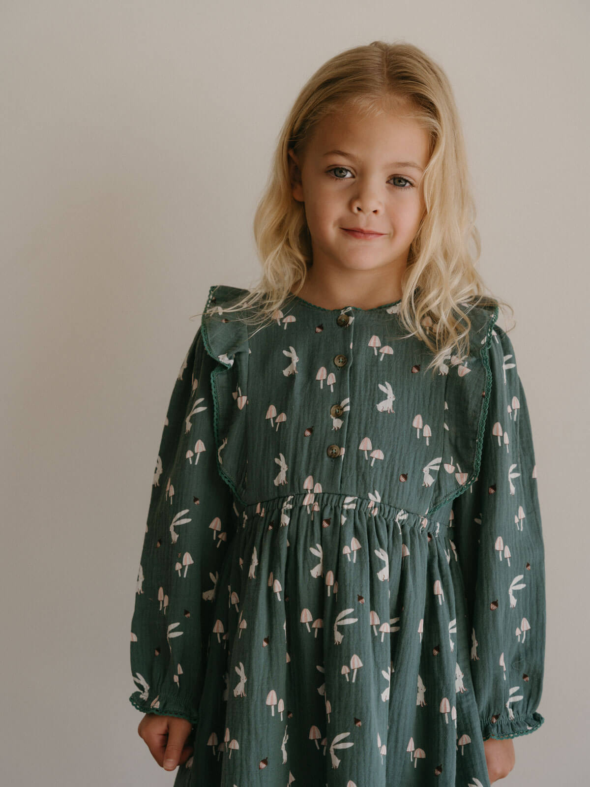 Young girl wearing a green dress with a pattern of small figures against a plain background Printed Woven Dress - Forest Gathering Balsam Girls