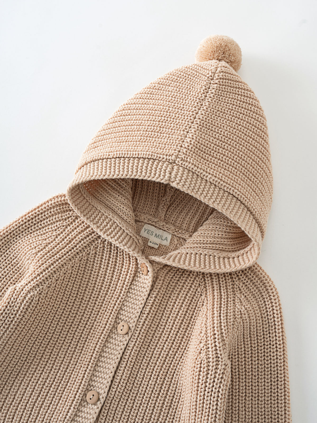 Beige knitted cardigan with hood and pompom laid flat on white surface Ribbed Hooded Cardigan - Clay Baby boy