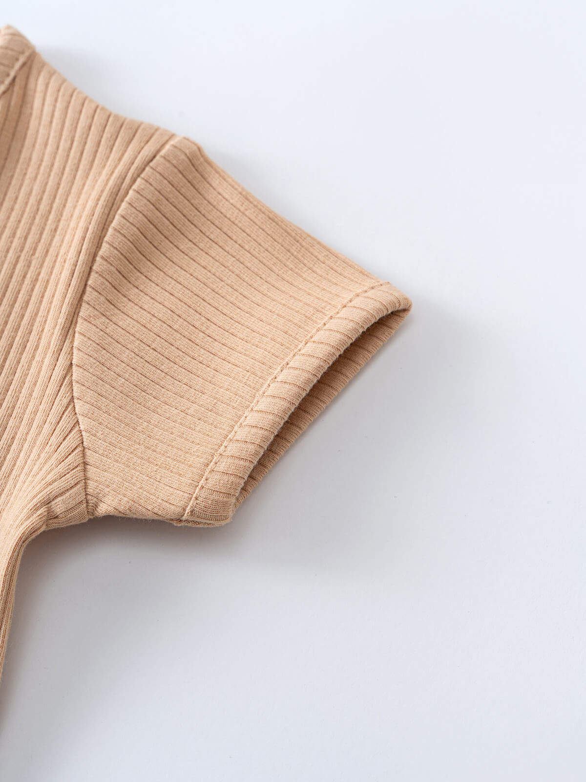 Close-up of beige ribbed knit fabric showing texture and finished edge detail Ribbed Short Sleeve One Piece - Sand Baby boy