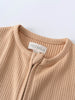Close-up of a beige ribbed garment with button detail and label Ribbed Short Sleeve One Piece - Sand Baby boy