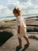 Child walking on rocks by the ocean with a cloudy sky.