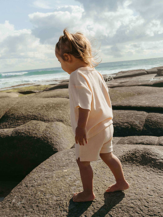 Child walking on rocks by the ocean with a cloudy sky.