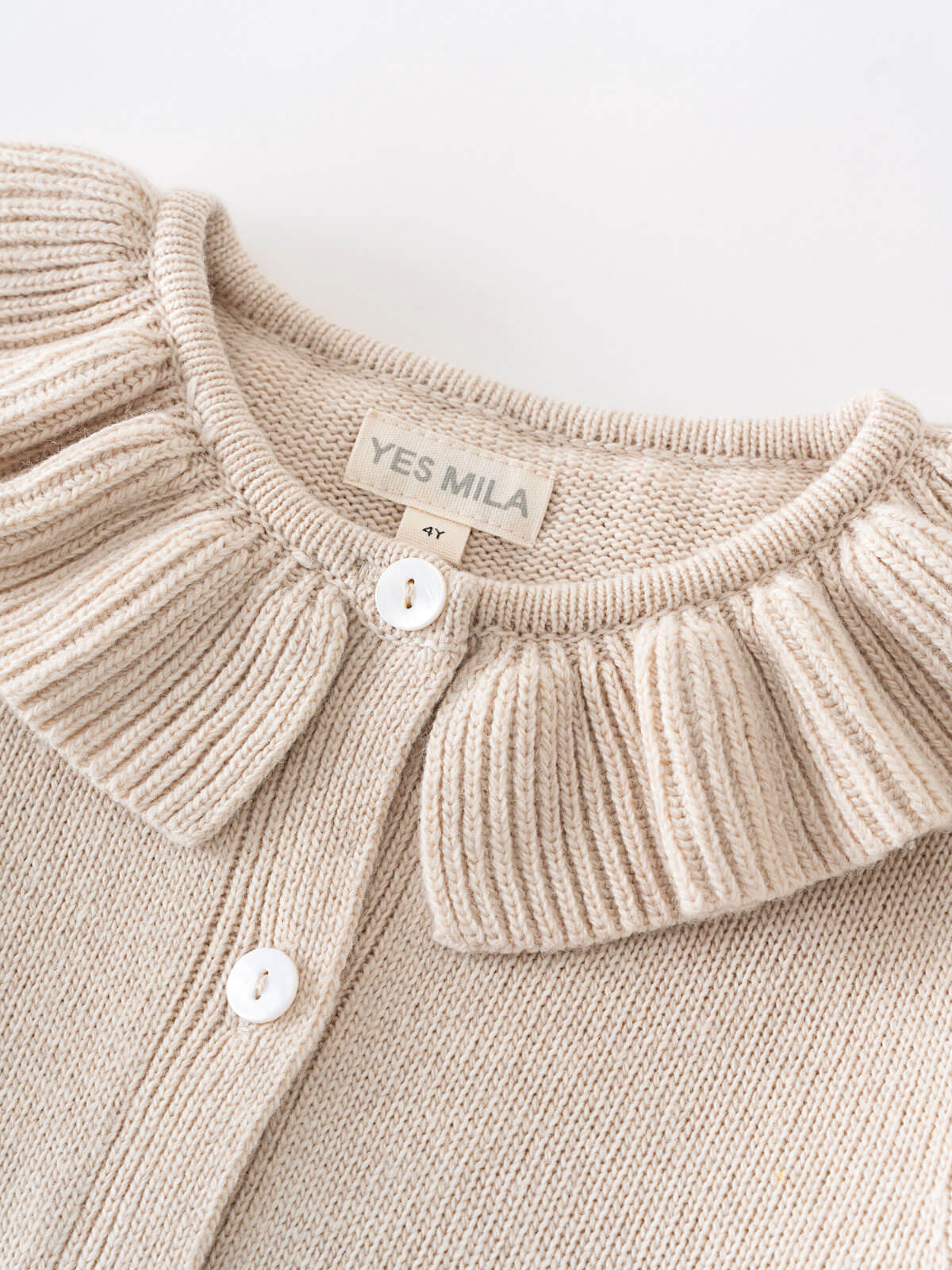 Beige knitted cardigan with a ruffled collar and visible 'YES MILA' label on a light background. Ruffle Cardigan - Ecru Girls