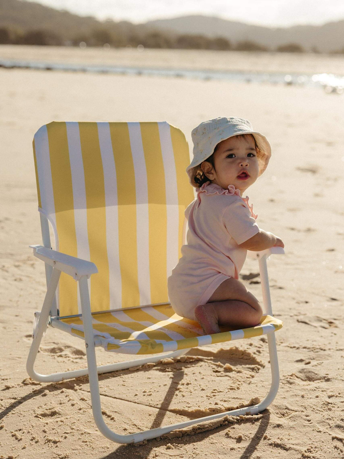 Baby girl wearing a soft pink bodysuit siting on a beach chair
