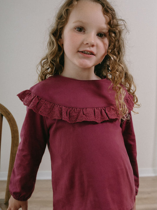 Young girl with curly hair wearing a plum-colored long-sleeved top with ruffled collar Ruffle Top - Plum Jam Girls