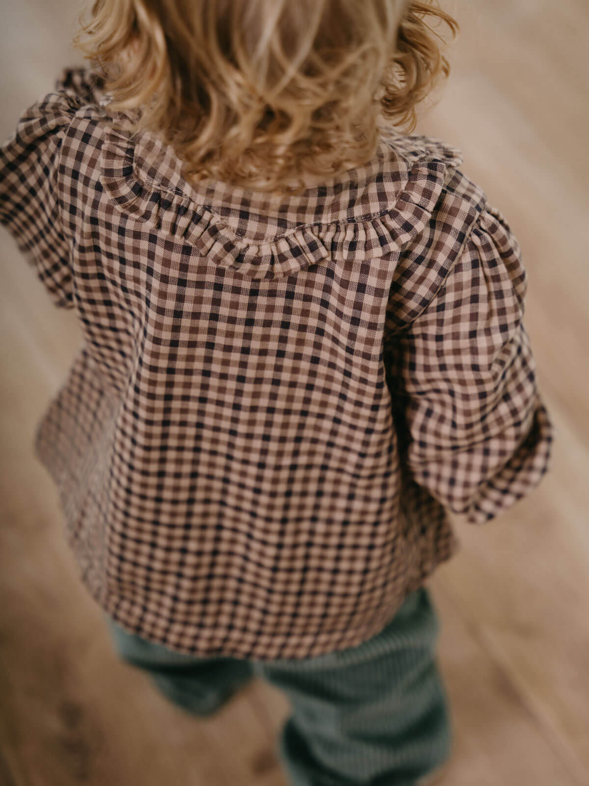 Child wearing a checkered shirt with ruffled shoulders in a natural setting Ruffle Woven Blouse - Muslin Cotton Check Girls