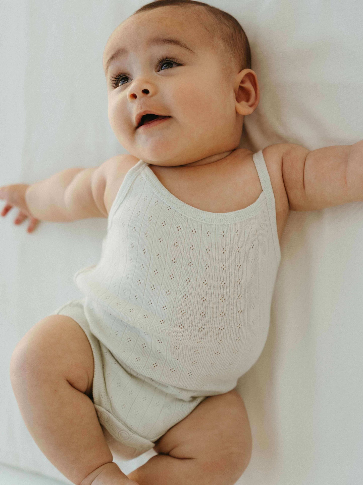 Baby wearing a light-colored sleeveless outfit on a white background