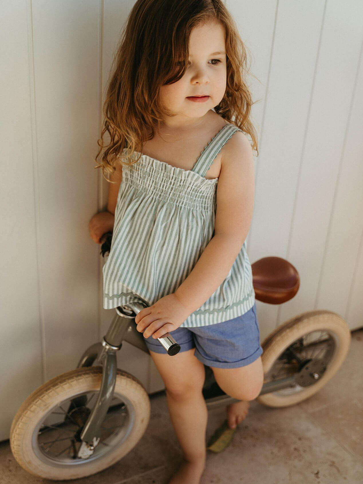 Young girl standing next to a balance bike indoors