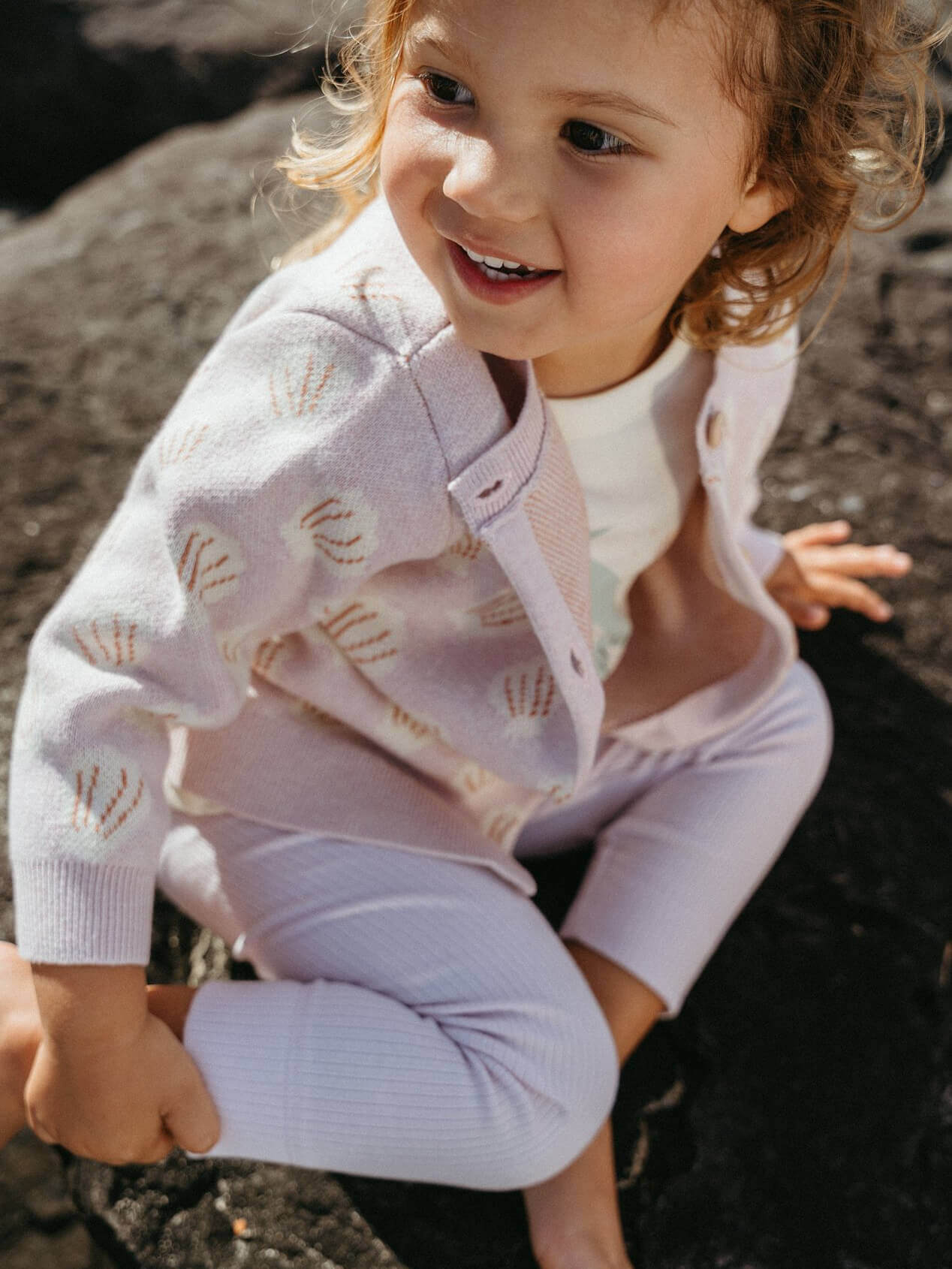 Child wearing a light purple outfit with a patterned cardigan outdoors.