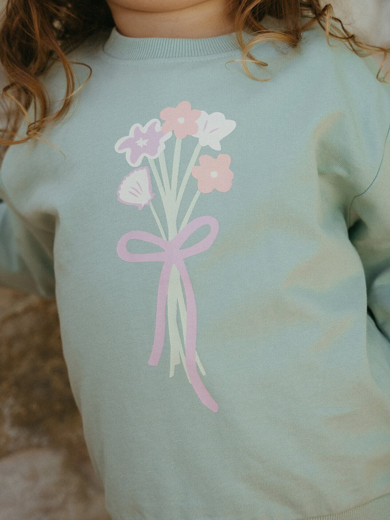 Light blue sweatshirt with pink flowers and a bow design on a blurred background
